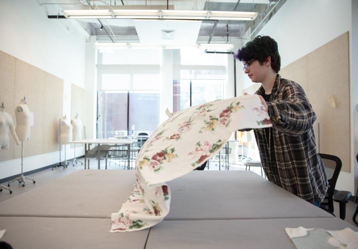 Student unfurling fabric onto a cutting table in the textiles studio