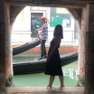 Silhouette of a woman standing in an archway in Venice, a gondolier paddles a boat behind her.