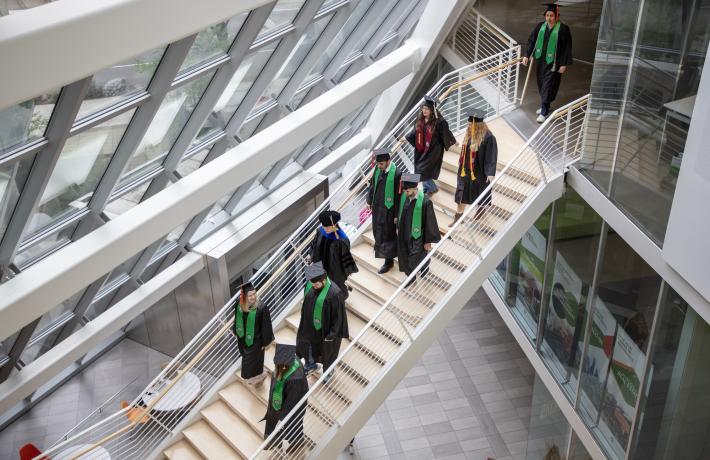 Graduating students in regalia descend stairs at Karl Miller Center