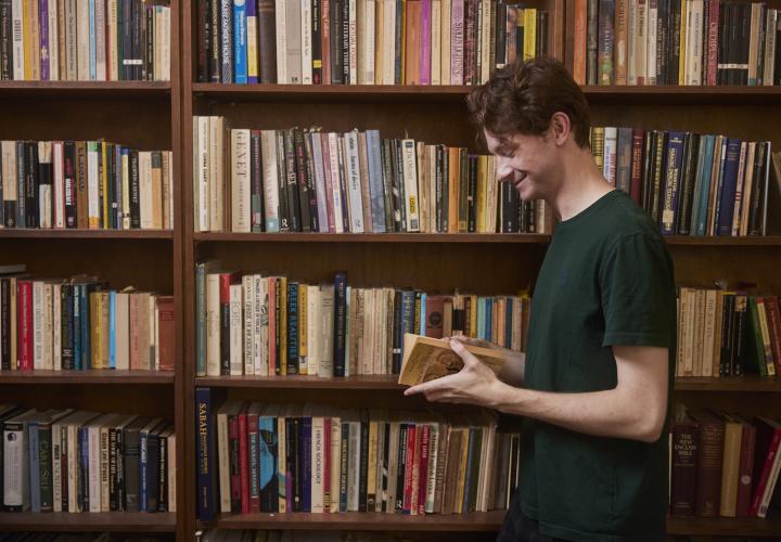 Man standing with book in hand in front of bookshelves