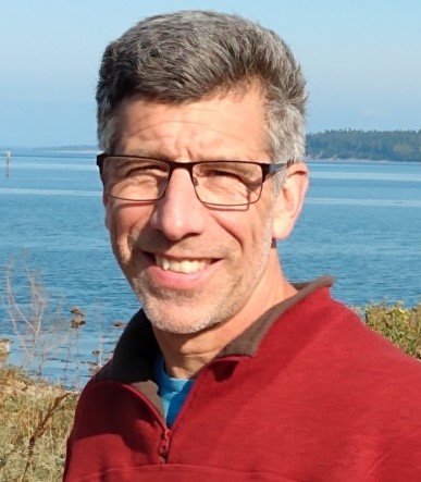 Photo of Randy Bluffstone in a red sweater, blue tee shirt in front of a body of water.