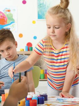 Three elementary school-aged children paint together in a colorful room.