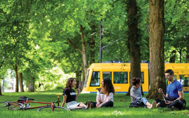 Four college students sit in a verdant park. Behind them is the Portland Streetcar.