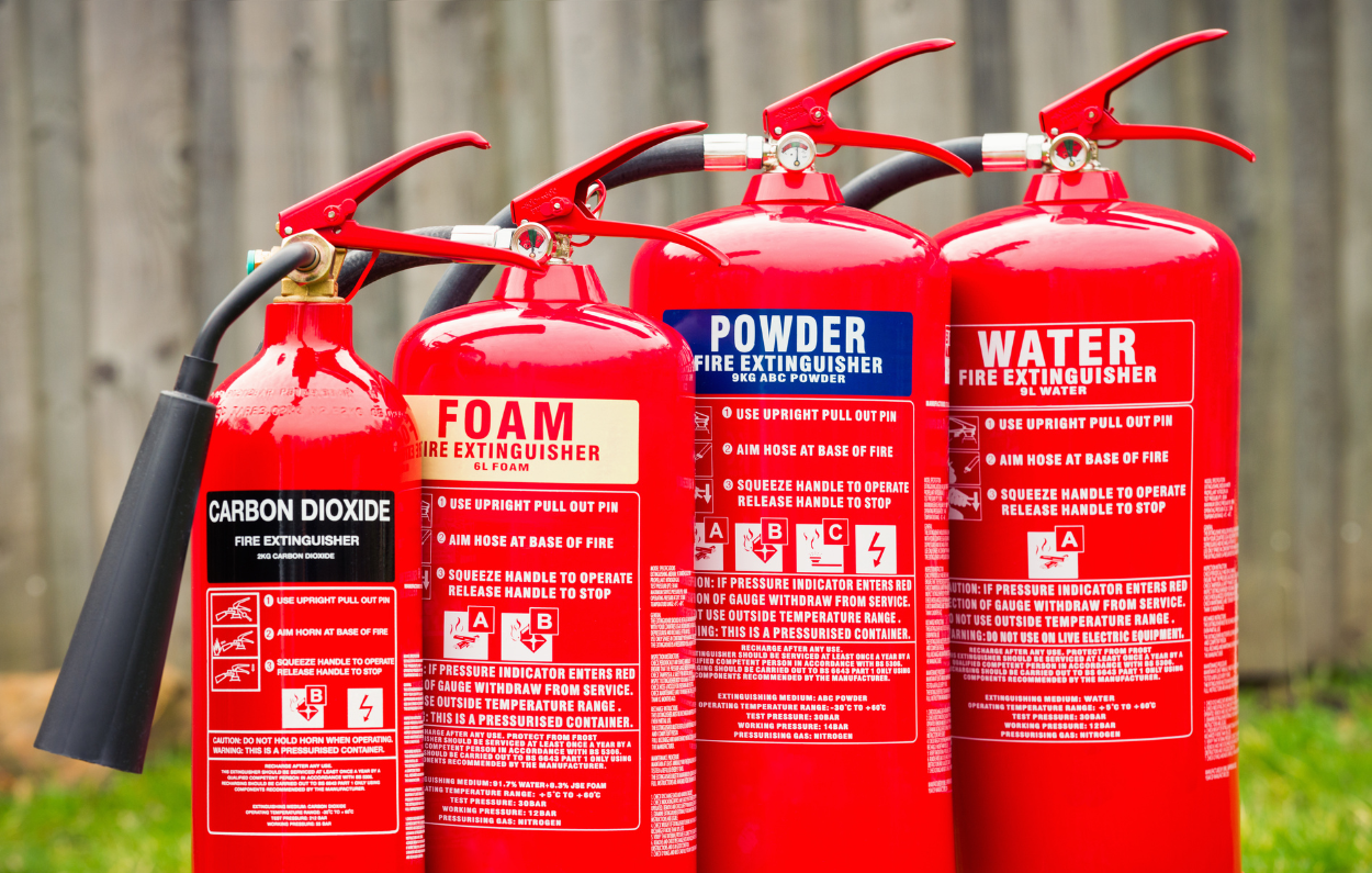 A row of four different types of fire extinguishers: CO2, foam, powder, and water