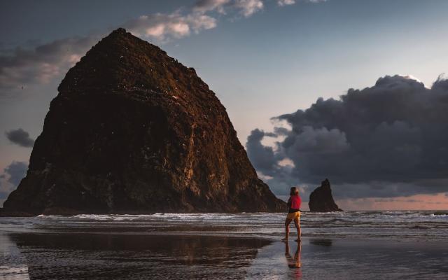 Person walking on beach with Haystack Rock in backdrop