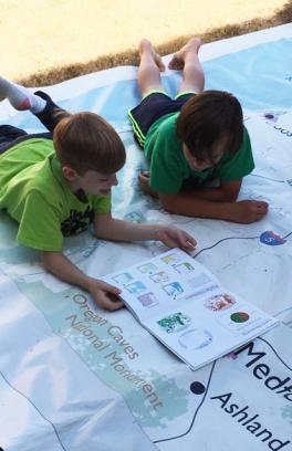 Two boys lying on a Giant Map of Oregon while looking at a Student Atlas of Oregon book.
