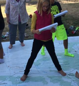 Girl standing on giant map reading student atlas