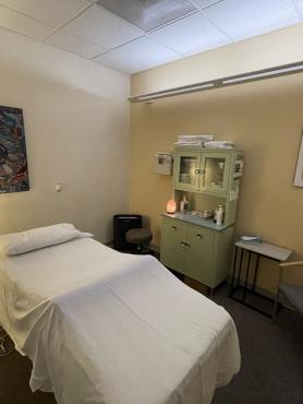 View of the acupuncture room with a bed, chair, lamp and pictures on the wall