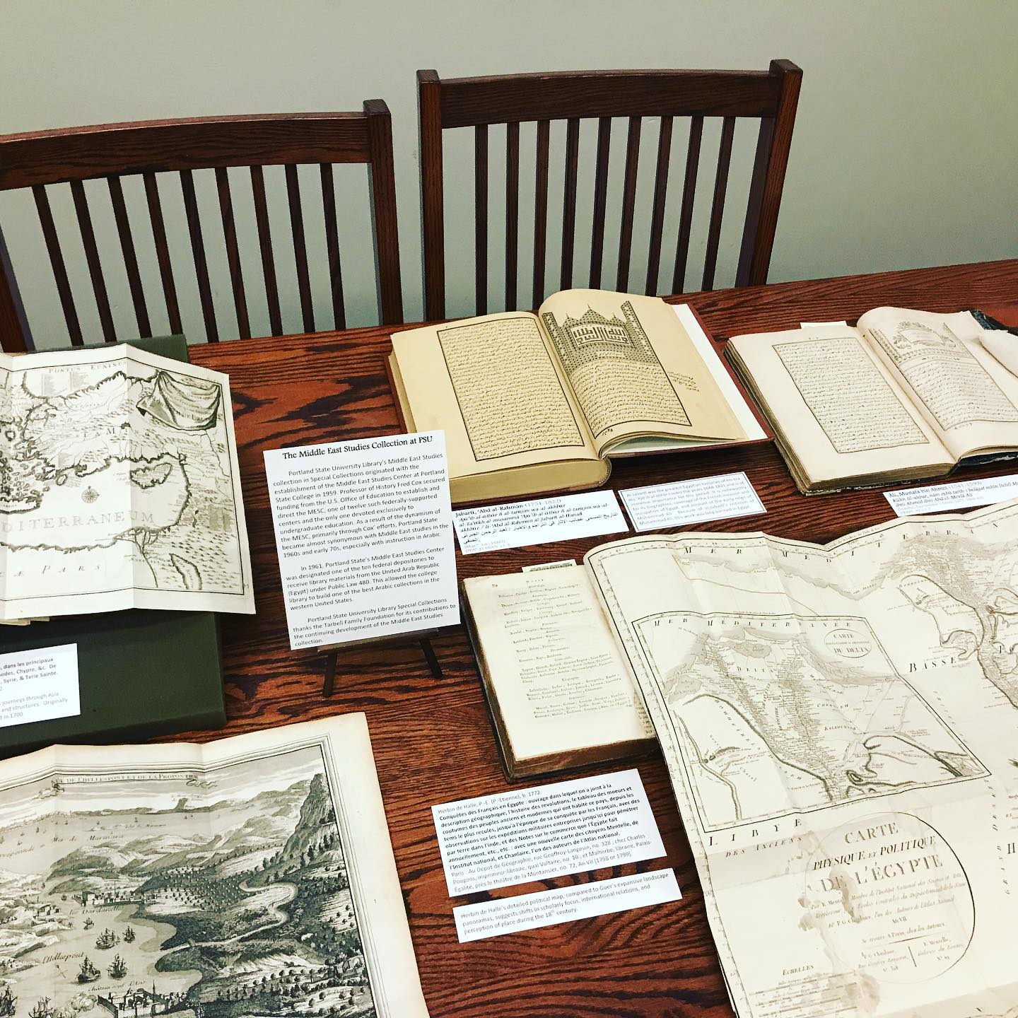 A collection of old books and maps on display on a wooden table. 