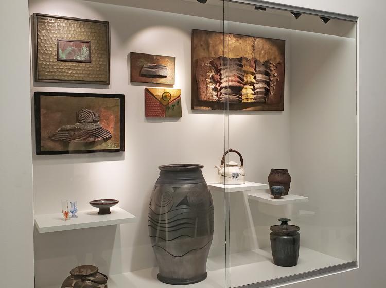 Display case in a hallway, with several works of ceramic and mixed media artwork in varying sizes, including pots as well as abstract wall-mounted art.