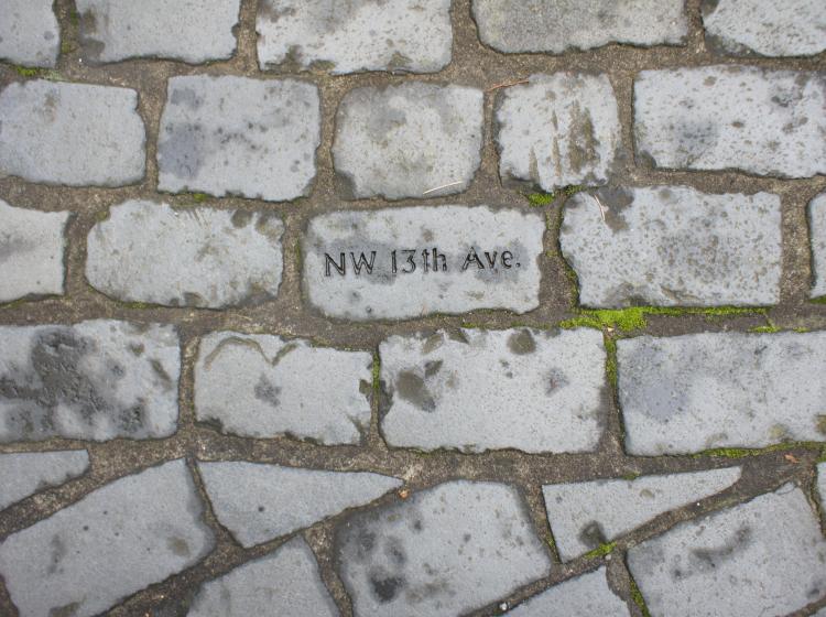 Close-up of cobblestones. "NW 13th Ave" is etched on the cobblestone at center.