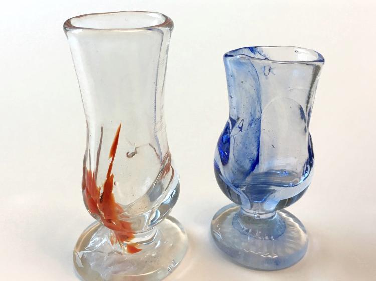Two small, clear glass goblets against a white background. The one at left is taller and includes red markings. The other is partly blue.
