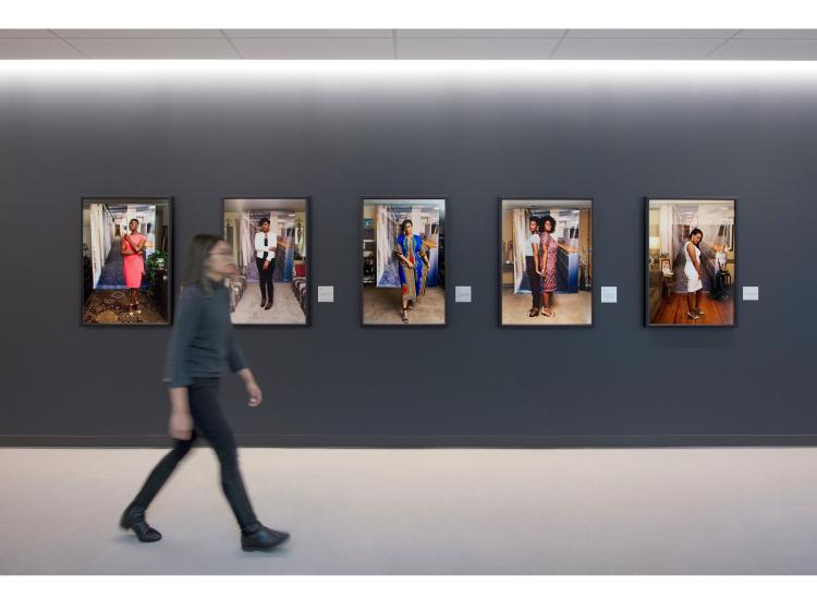 All five of the previous photos are shown framed on a dark grey wall, with descriptive plaques next to them. A person is walking in the foreground.