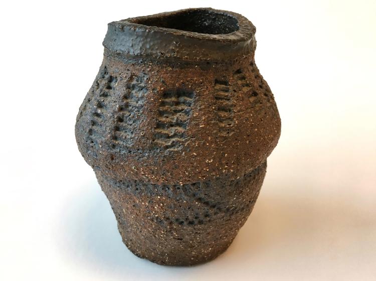 A large brown ceramic vase, irregular in shape, with a pattern of lines embossed into the surface