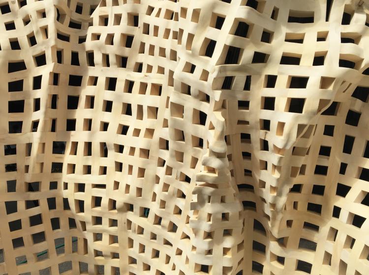 Close-up showing the texture of the wooden sculpture’s surface, a grid-like structure with undulating contours.