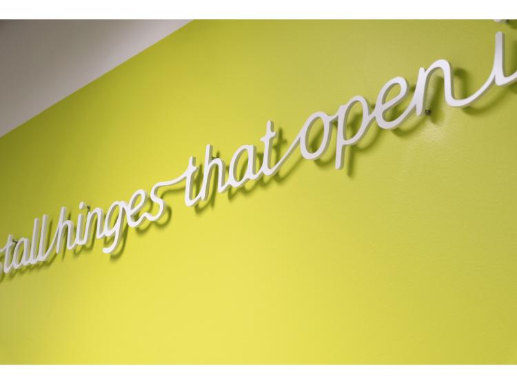 Close-up showing raised text that floats about an inch from a green wall, casting a shadow. The visible portion of text reads "hinges that open."