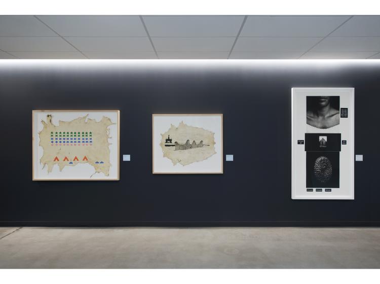 Three framed pieces of art are seen in a dark grey hallway. From left to right: Space Invaders by Leonard Getinthecar, Natural Resources by Leonard Getinthecar), and Counting by Lorna Simpson.
