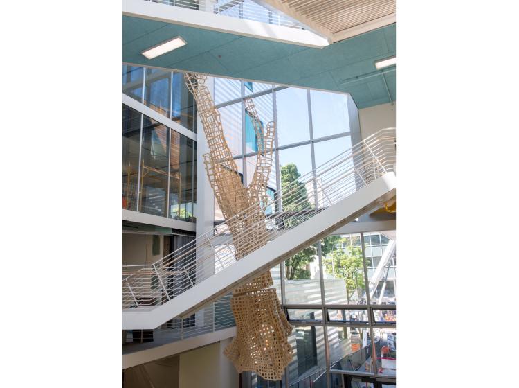 The sculpture is seen hanging in the atrium of Karl Miller Center, behind a staircase and an elevated walkway.