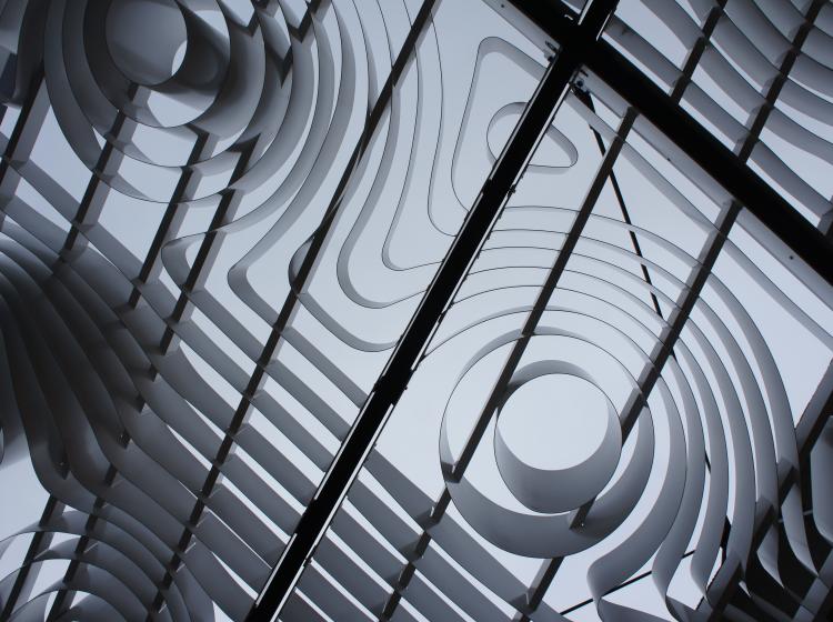 View directly up through the grid of curving slats. Blue sky is visible through the delicate curving grid structure.