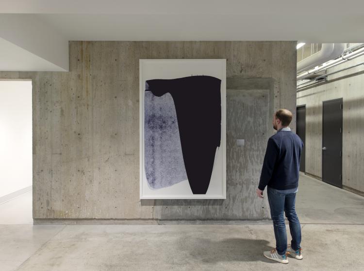 The artwork is seen on a concrete wall in Peter Stott Center, with a person standing in the foreground, looking at it.