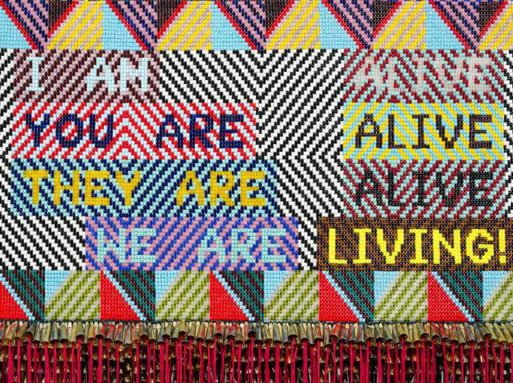 Detail image of the artwork, focused on the area with text. The text and patterned background are made up of a variety of contrasting colors.