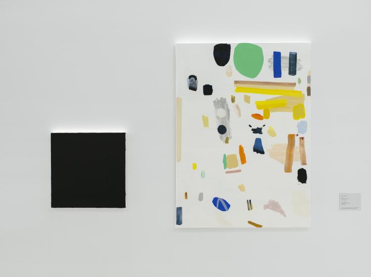 A pair of paintings side by side. The one on the left is smaller and solid black; the one at right is white with colorful abstract shapes