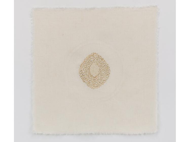 Stiched artwork with a small oval-shaped area of gold and white stitching at center, on off-white background