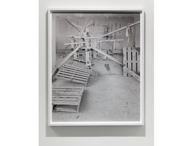 Black and white framed photograph depicting varoius "barricade" items (wood, tires) arranged in front of a backdrop that is another photo of the same materials, creating an illusion of continuation