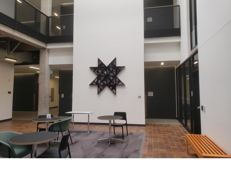 The artwork is seen installed on a white wall, in a wide shot showing the third floor study lounge in Fariborz Maseeh Hall