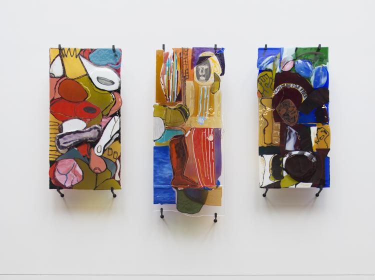 Three abstract 2-dimensional multicolored glass artworks are seen side-by-side against a white wall