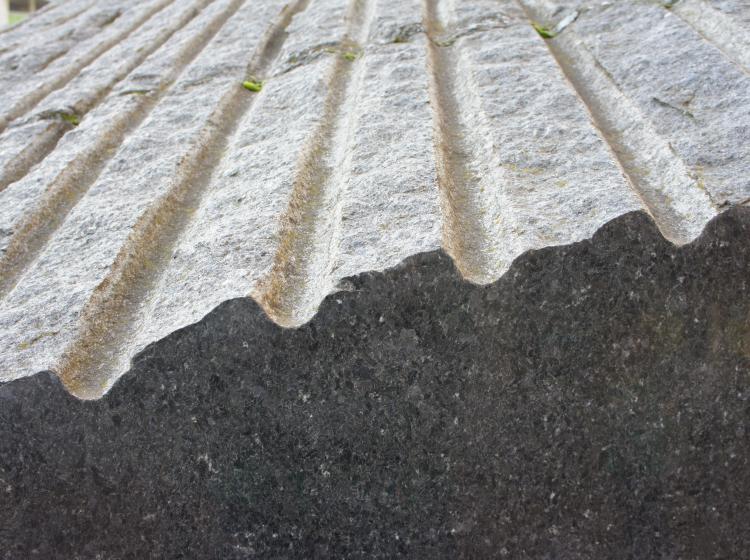 Close-up of a granite sculpture, showing the ridged texture on the top surface in contrast to the shiny, smooth texture of the side facing the viewer
