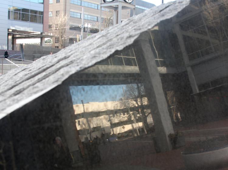 Close-up shot of the shiny side of the darker colored sculpture. The Recreation Center building is visible in the background, and the Urban Center building is reflected on the side of the sculpture