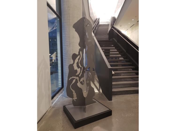 Sculpture of an abstracted human figure, composed of three conjoined black two-dimensional "cutout" elements, viewed from another angle