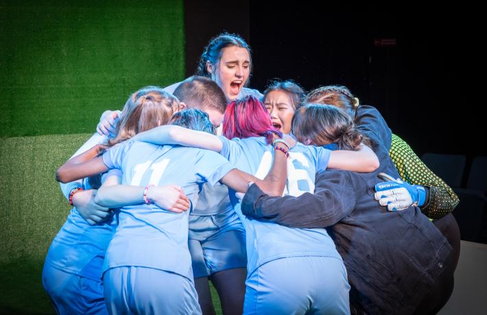 Cast of PSU Theater's "The Wolves" dressed in soccer costumes in a huddle cheer.