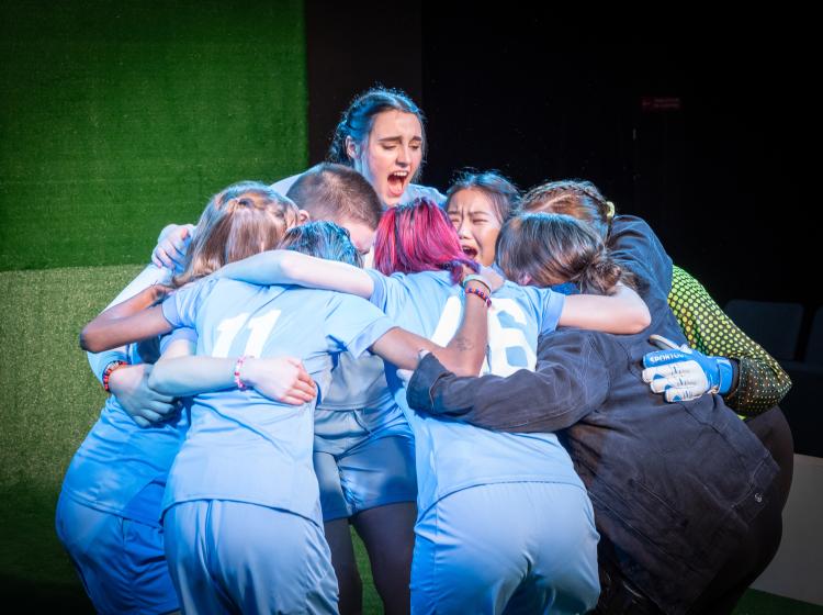 Cast of PSU Theater's "The Wolves" dressed in soccer costumes in a huddle cheer.