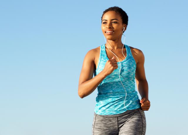 Person running outdoors with sun on their face and earbuds in their ears. The background is blue, like a clear blue sky.
