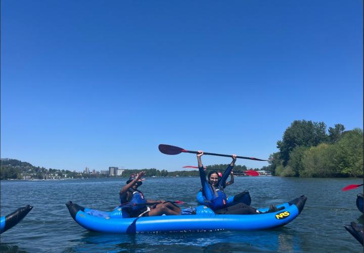 Two people kayaking on the sunny Willamette river. One person raising their paddle in the air