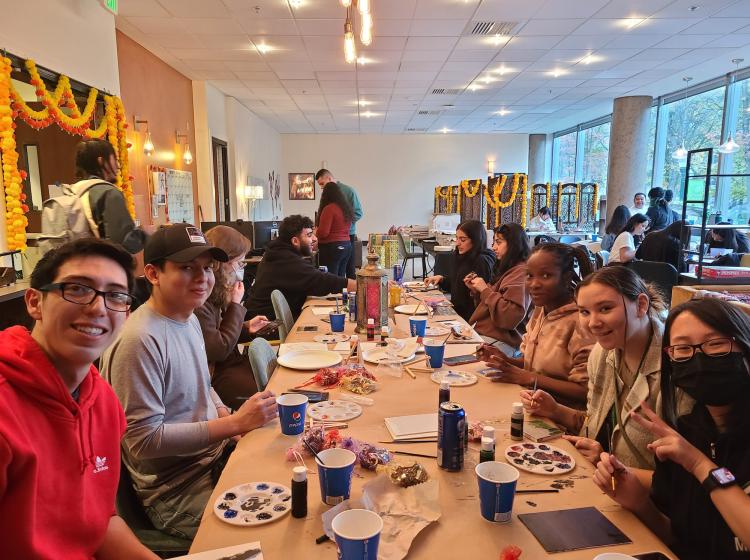 A group of students gather around a long table and smile at the camera 