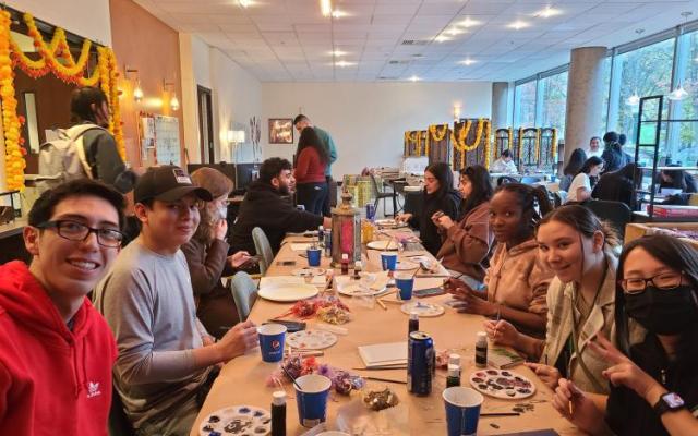 A group of students gather around a long table and smile at the camera 