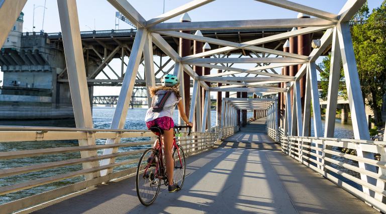A PSU student riding a bike through a bridge bike path next to the river.