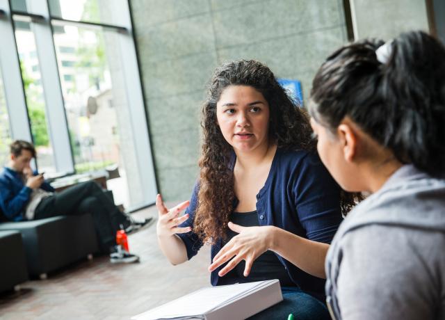 Two students sitting and talking. One student is gesturing.