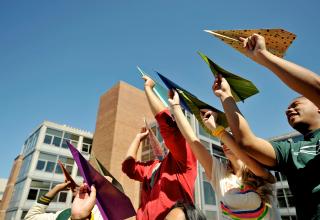 Group of students holding multicolored paper airplanes in the air.