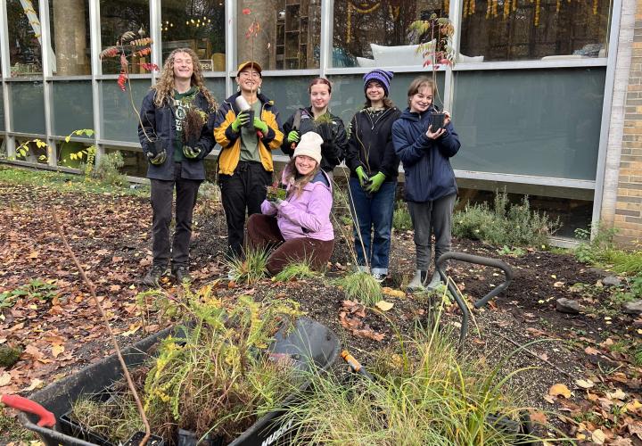 A group of people are standing in a garden behind wheelbarrrows full of plants.