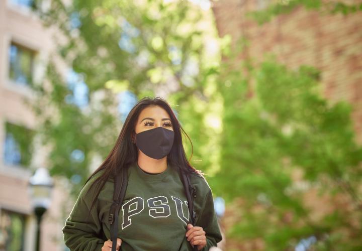 Student wearing mask walking across PSU campus.