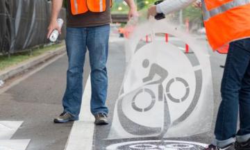 People stand on a street painting a bicycling symbol onto it.